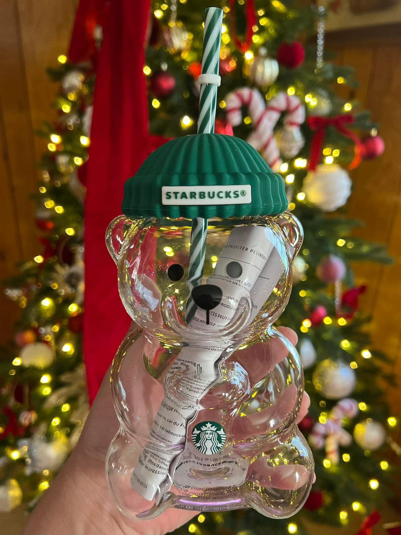 Clear bear-shaped Starbucks cup with green lid and straw against a festive Christmas tree background